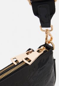 Borsa in pelle laccata nera con hardware in tono oro, doppie cerniere, motivi in rilievo e tracolla removibile. Design compatto e strutturato.