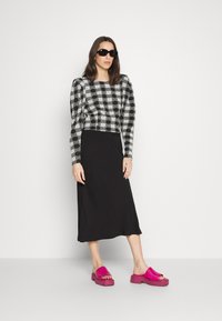 Top de manga longa xadrez em preto e branco combinado com uma saia midi preta e sandálias de plataforma rosa. Óculos de sol completam o visual.