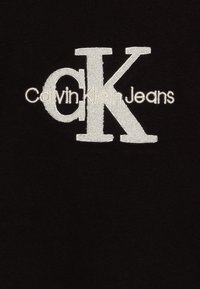 Camiseta de algodón negra con un gran logotipo bordado en blanco que dice "Calvin Klein Jeans" y un diseño estilizado de "CK".