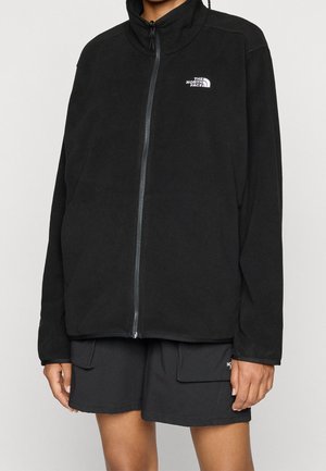 Personne portant une veste polaire noire zippée et un short cargo noir avec le logo The North Face sur les deux vêtements.
