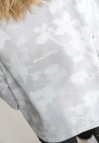 Jasnoszara bluza z kwiatowym wzorem oraz napisem "MULTIPLY" w kolorze białym. Miękka tkanina, luźny krój i gładka faktura.