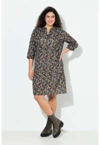 Blumenmuster-Kleid in Marineblau, Gelb und Beige; mit 3/4-Ärmeln, mittlerer Oberschenkellänge und lockerer Passform. Kombiniert mit schwarzen Schnürstiefeln.