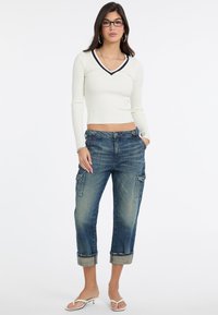 Weißes, geripptes Langarmoberteil mit V-Ausschnitt, kombiniert mit lässigen, hellblauen Cargo-Jeans im Relaxed Fit, die Seitentaschen und umgeschlagene Säume haben.