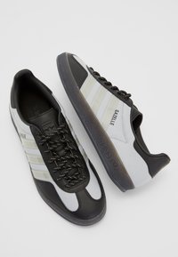 Fekete-fehér Adidas Gazelle sportcipők texturált felsőrészzel, három oldalsó csíkkal és egy diszkrét árnyalatú gumi talppal rendelkeznek.