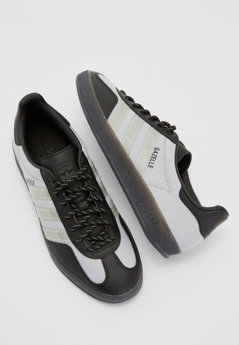 Schwarz-weiße Adidas Gazelle Sneakers verfügen über ein strukturiertes Obermaterial, drei seitliche Streifen und eine Gummisohle mit einem subtilen Farbverlauf.