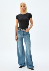 Sort kortærmet bodysuit parret med lyseblå brede jeans, med et sort bælte med sølvhardware. Glatte teksturer og afslappet design.