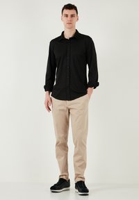 Zwarte longsleeve shirt met knoopsluiting, beige slim-fit broek en zwarte sneakers. Het shirt heeft een kraag en opgerolde mouwen.