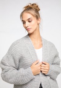 Hellgraue Strickjacke mit einer weichen, strukturierten Oberfläche, offener Vorderseite und weiten Ärmeln. Sie verfügt über ein Rippmuster und keine sichtbaren Verschlüsse.