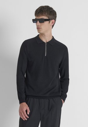 Pullover nero in maglia con colletto a mezza zip e maniche raglan testurizzate. Il modello indossa occhiali da sole neri angolari. Design semplice e elegante.