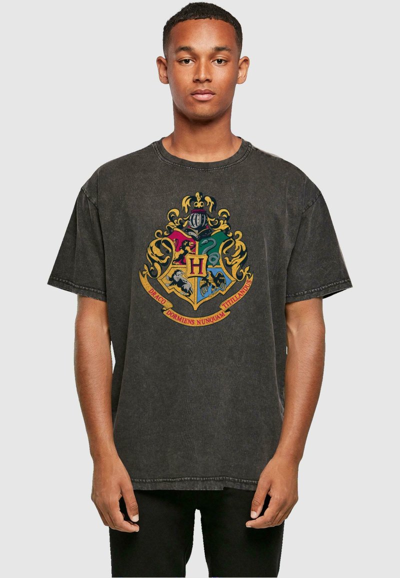T-shirt en coton noir avec une texture usée, présentant un graphic coloré du blason de Poudlard au centre. Manches courtes et col rond.