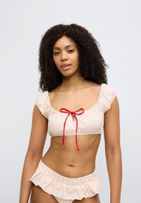 Σετ μπικίνι με κόκκινες και λευκές πουά, που περιλαμβάνει ένα κοντό τοπ με φιόγκο και βολάν στις άκρες του κάτω μέρους. Απαλή υφή υφάσματος.