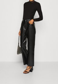 Zwart geribd top met lange mouwen en kanten accenten; hooggetailleerde zwarte leren broek met wijde pijpen; sandaaltjes met transparante bandjes en hak; handtas met kralen.