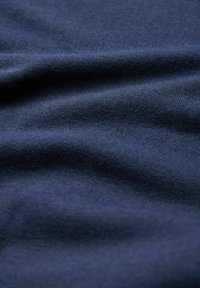 Tissu bleu marine avec une texture lisse, présentant de légères ondulations et plis, indiquant l'élasticité et la douceur dans le design textile.