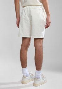 Witte katoenen heren shorts met een elastische tailleband, platte voorkant, zijzakken en een achterzak, gecombineerd met witte sneakers en sokken.