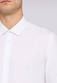 Witte button-up shirt met een klassieke kraag, subtiele textuur en een klein geborduurd logo op de borst. Glad materiaal met een nette afwerking.
