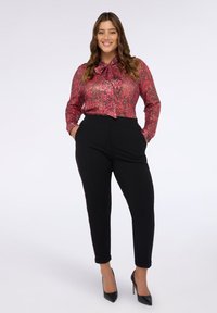 Blusa a maniche lunghe rossa e rosa con un colletto a fiocco, abbinata a pantaloni neri tapered e tacchi alti neri. Tessuto liscio in tutto.