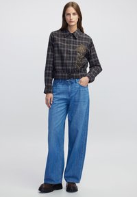 Camicia a quadri ritagliata in blu scuro e marrone, decorata con ornamenti floreali; abbinata a jeans larghi blu chiaro e calzature nere spesse.