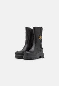 Black leather ankle boots with a side zipper, chunky rubber sole, and a gold logo accent. Smooth texture with a sleek design.