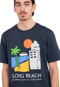Marine katoenen t-shirt met een kleurrijke afbeelding van een strandscene met een palmboom, boot, gebouwen en een zon, met de tekst "LONG BEACH."
