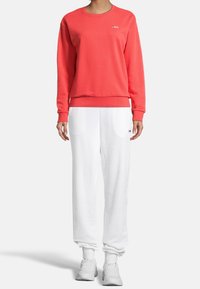 Sudadera roja con cuello redondo y puños acanalados, combinada con pantalones deportivos blancos de corte relajado y bolsillos laterales. Ambos confeccionados en algodón.