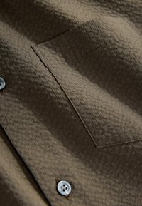 Braunes, strukturiertes Hemd mit kariertem Muster, einer Brusttasche und silbernem Knopfdetail. Weicher Stoff mit glatter Oberfläche.