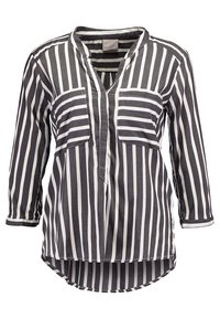 Blusa a maniche lunghe a righe bianche e nere con scollatura a V, due tasche sul petto e orlo curvo. Realizzata in un tessuto leggero con una texture liscia.