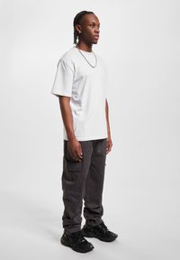 Camiseta blanca de manga corta, pantalones cargo grises sueltos con bolsillos, zapatillas negras y una cadena plateada. Diseño simple, ajuste relajado y estilo casual.