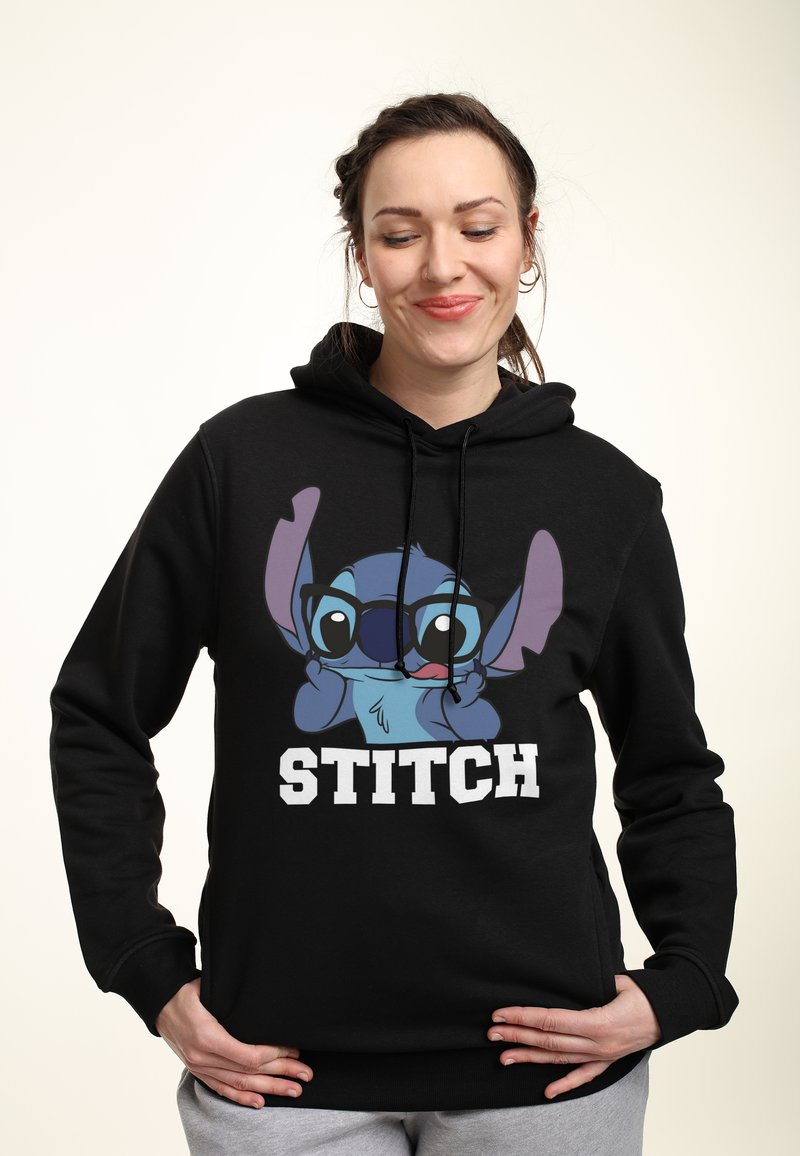 Černá mikina s kapucí s velkým potiskem modré postavy s brýlemi a nápisem "STITCH" tučným bílým písmem ve spodní části.