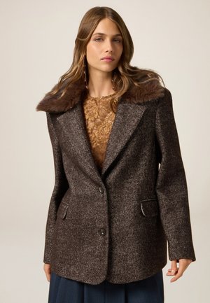 Brązowy płaszcz wełniany w wzór jodełki z kołnierzem z sztucznego futra, dwoma przednimi kieszeniami i dopasowanym krojem. Posiada zapięcie na jeden guzik.