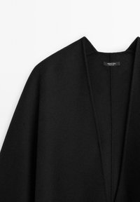 Černý kardigan z vlněné směsi s výstřihem do V a otevřeným předním dílem. Má měkkou texturu a minimální švy, označen "Massimo Dutti."