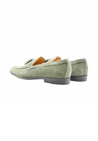 Mocassini verdi in suede con una texture liscia, tacco basso in gomma nera e design slip-on, caratterizzati da cuciture decorative e piccoli dettagli.