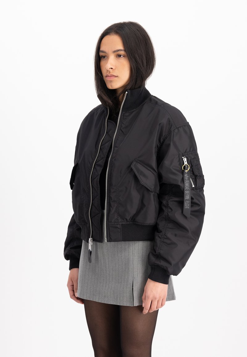 Chaqueta bomber negra con cremallera frontal, puños elásticos y un bolsillo parche en la manga. Tejido suave y diseño corto.