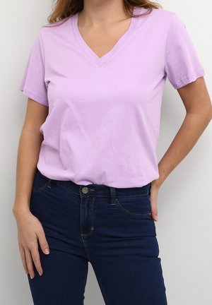 T-shirt lilas à col en V en coton doux, avec des manches courtes et une coupe décontractée, associé à un jean skinny bleu foncé.