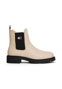 Bottine en cuir beige à panneau latéral élastique noir, semelle crantée noire, doublure en fourrure synthétique et patch logo Tommy Jeans sur le côté.
