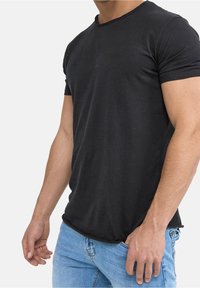 Schwarzes Baumwoll-T-Shirt mit kurzen Ärmeln und rundem Halsausschnitt, das eine lockere Passform und leichte Abnutzung am Kragen aufweist.