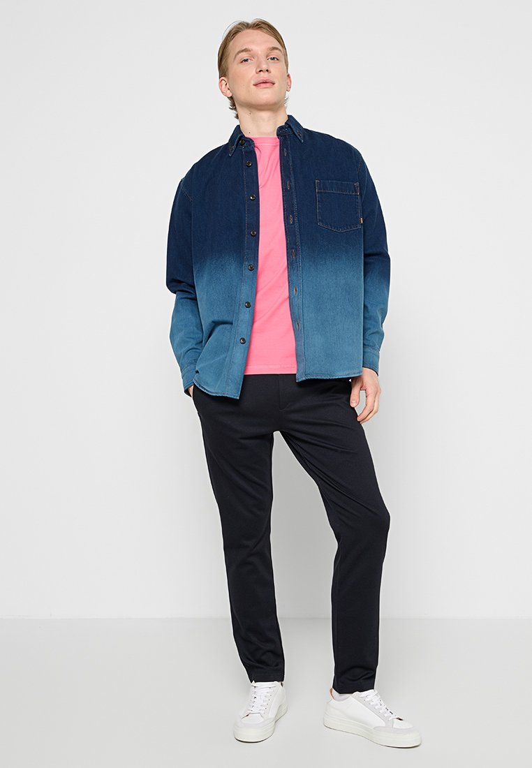 Koszula dżinsowa z gradientem od ciemnoniebieskiego do jasnoniebieskiego, na różowej koszulce, w połączeniu z ciemnymi spodniami i białymi trampkami.