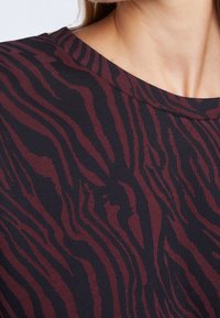 Tessuto nero con un motivo a strisce zebra bordeaux. Presenta una texture liscia e una scollatura ampia. Dettaglio ravvicinato del materiale.