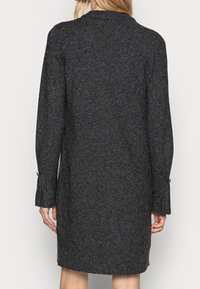 Robe en laine gris charbon à manches longues et coupe décontractée. Présente des accents de boutons aux poignets et une texture en tricot côtelé.