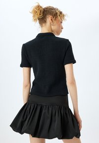 Svart kortärmad topp med texturerat material och en något cropped design, matchad med en svart voluminös kjol med volangdetaljer.