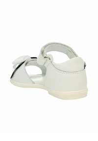 Sandalino bianco per neonati con lati aperti, una cinghia sul retro con chiusura in Velcro e un fiocco decorativo bianco sulla parte anteriore.
