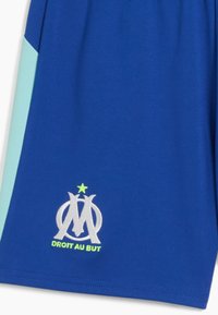 Zili sporta šorti zilā krāsā ar baltu un zaļu Olimpique de Marseille logo un devīzi "DROIT AU BUT" tuvumā apakšmalai.