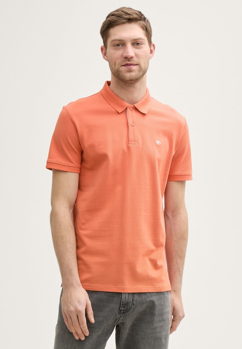 Herrars kortärmad polo skjorta i korallorange bomull, med klassisk krage och tre-knappsstängning, samt en liten logotyp på bröstet.
