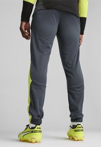 Grijze sportbroek met gele accenten en geribbelde manchetten, gecombineerd met gele voetbal-schoenen met zwarte details en het "KING"-merk.