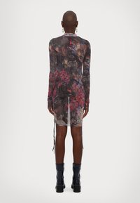 Robe à manches longues en tissu transparent à motifs avec des nuances sombres tourbillonnantes et des accents floraux. Présente des liens sur les côtés et un dos transparent.