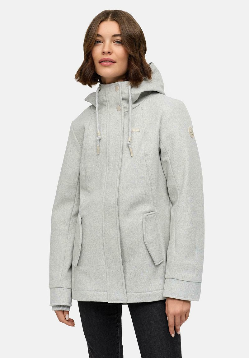 Donna che indossa un cappotto invernale grigio chiaro con cappuccio, tasche frontali, stringhe e pantaloni neri su uno sfondo uniforme.