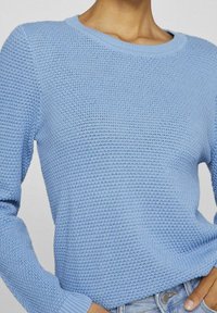 Hellblauer Strickpullover mit strukturiertem Muster, rundem Ausschnitt und langen Ärmeln. Der Stoff wirkt weich und dehnbar.