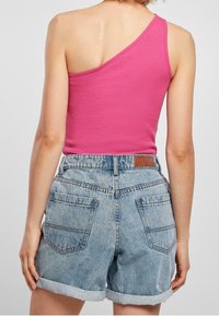 Top rosa de un solo hombro combinado con pantalones cortos de mezclilla de lavado medio que cuentan con dobladillos enrollados y bolsillos traseros. Diseño sencillo con un ajuste casual.
