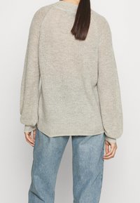 Light grey knitted sweater with a textured finish, puffed sleeves, and a rounded hem, paired with loose blue denim pants.