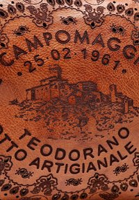 Oggetto in pelle marrone con testo in rilievo "CAMPOMAGGI 25.02.1961" e un'illustrazione di un edificio, circondato da un bordo decorativo.