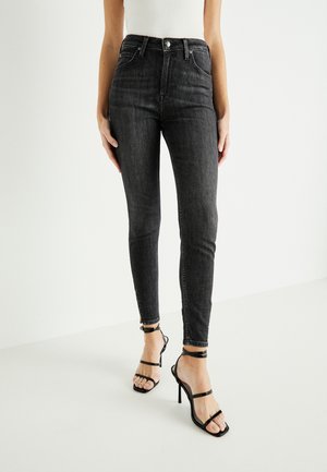 Czarne jeansy skinny o wysokim stanie wykonane z denimu, z pięcioma kieszeniami, delikatnym wyblaknięciem i dopasowanym krojem, zestawione z czarnymi sandałami na obcasie.